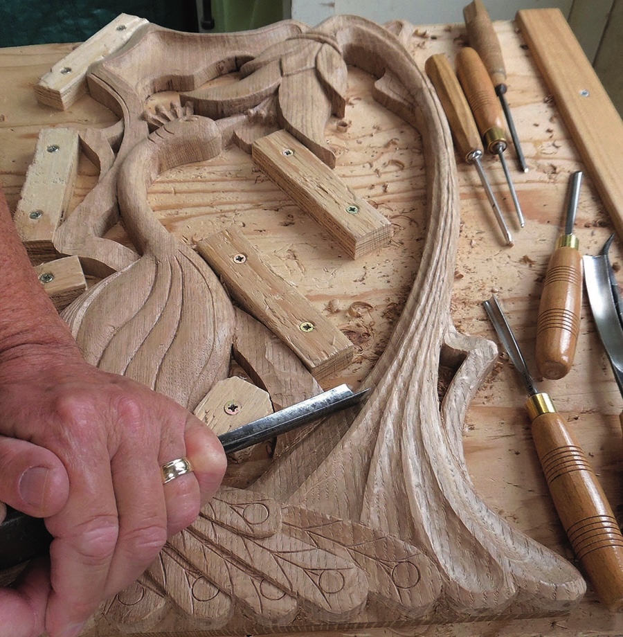 Hand carving intricate wooden art piece on workbench.