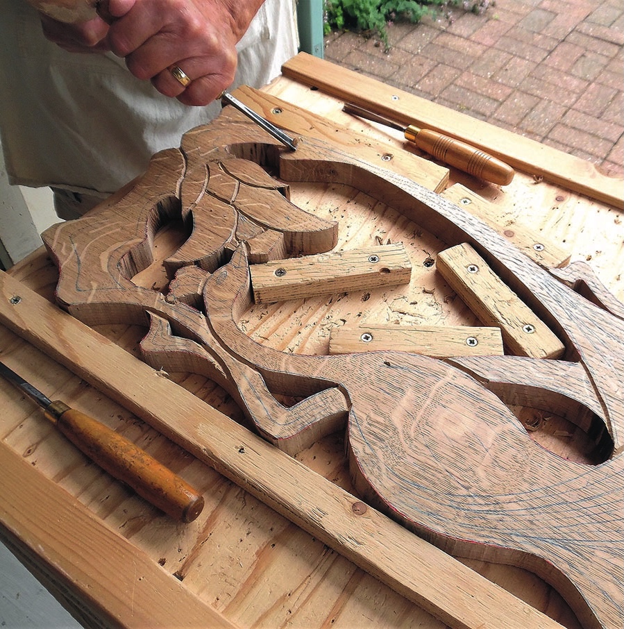Person carving intricate wooden design on workbench.