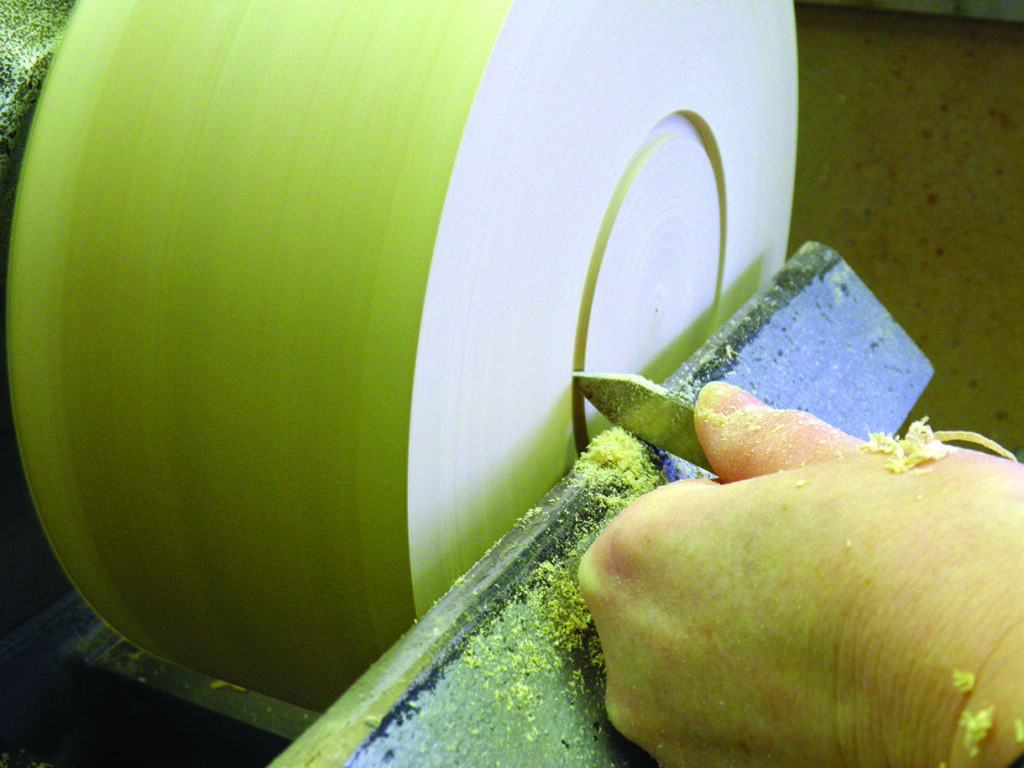 Hand using chisel on wood lathe.