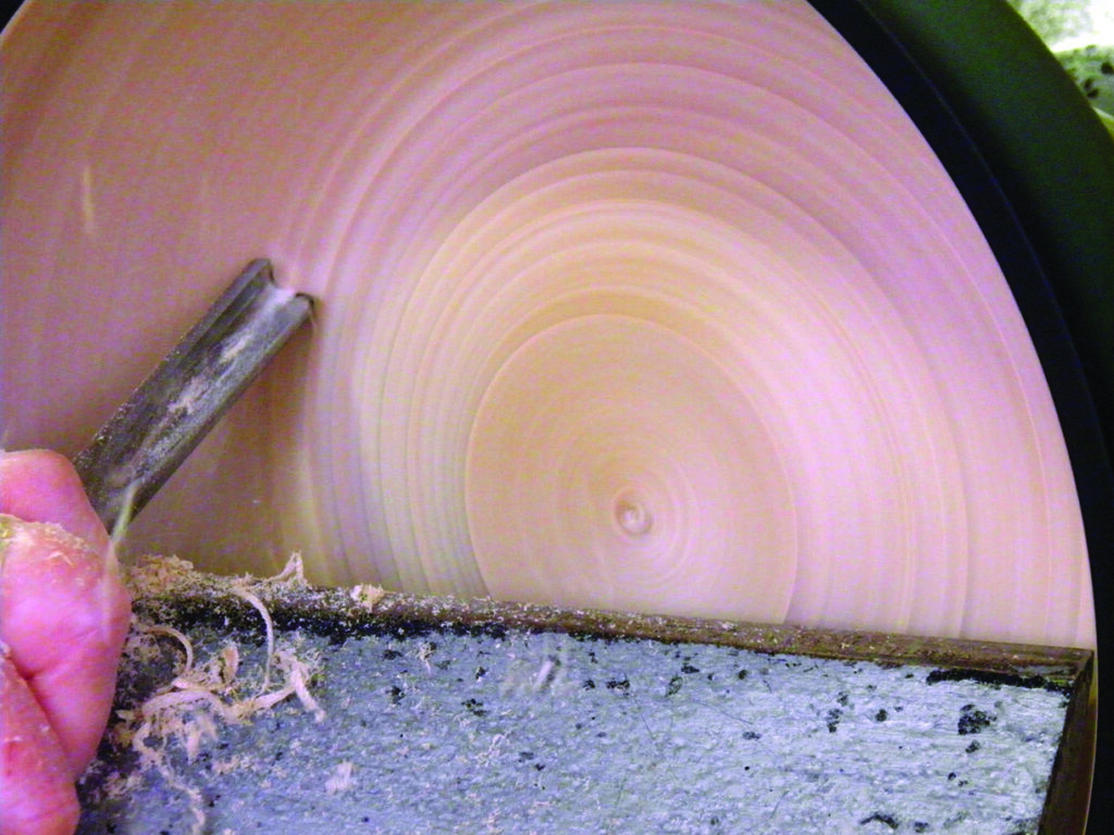 Wood lathe turning with chisel and shavings.