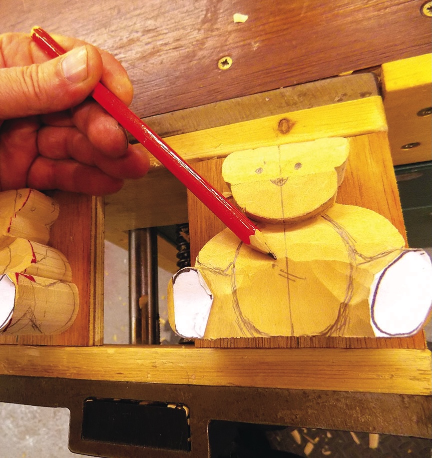 Person sketching wooden teddy bear with red pencil