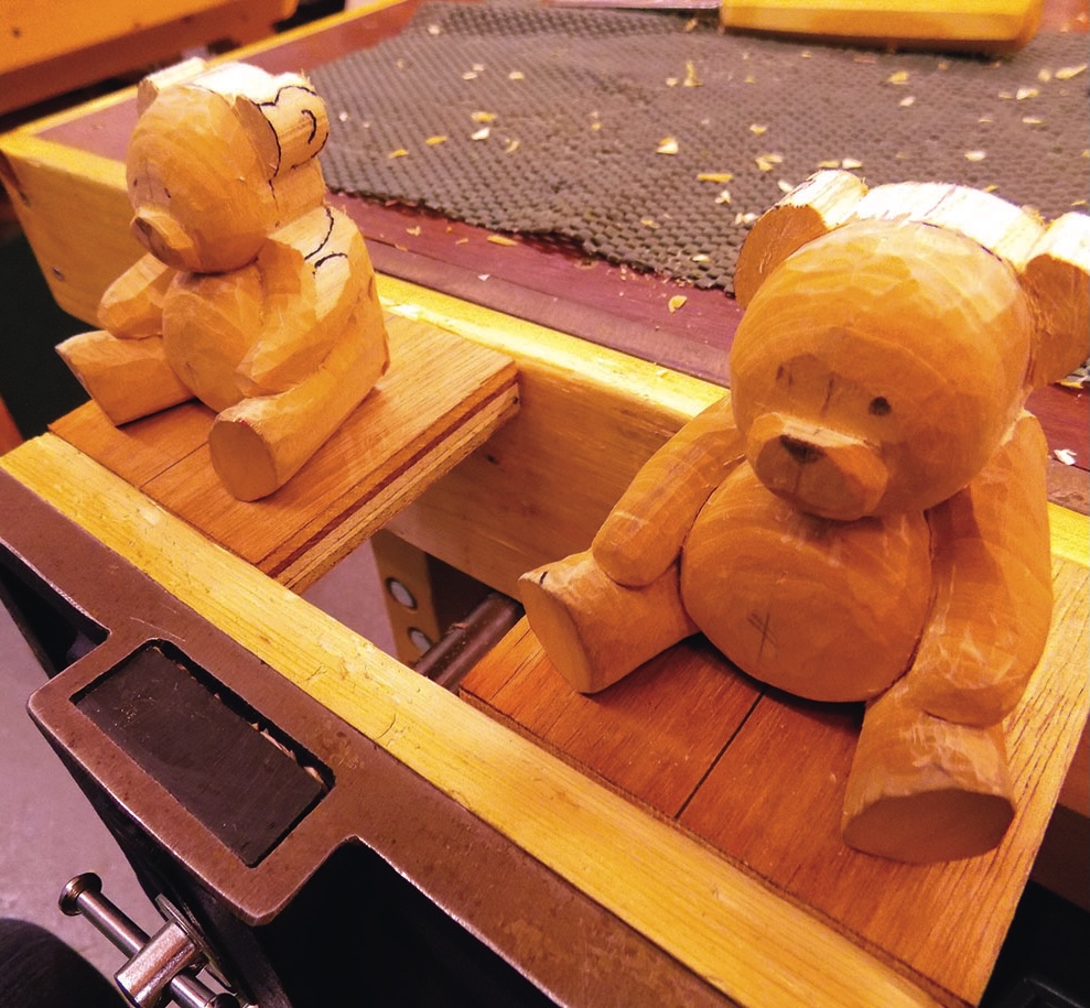 Two carved wooden bears on a workbench.