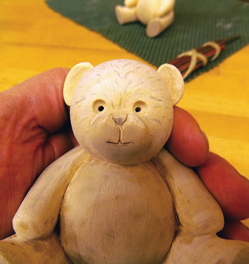 Hand holding carved wooden teddy bear figurine.