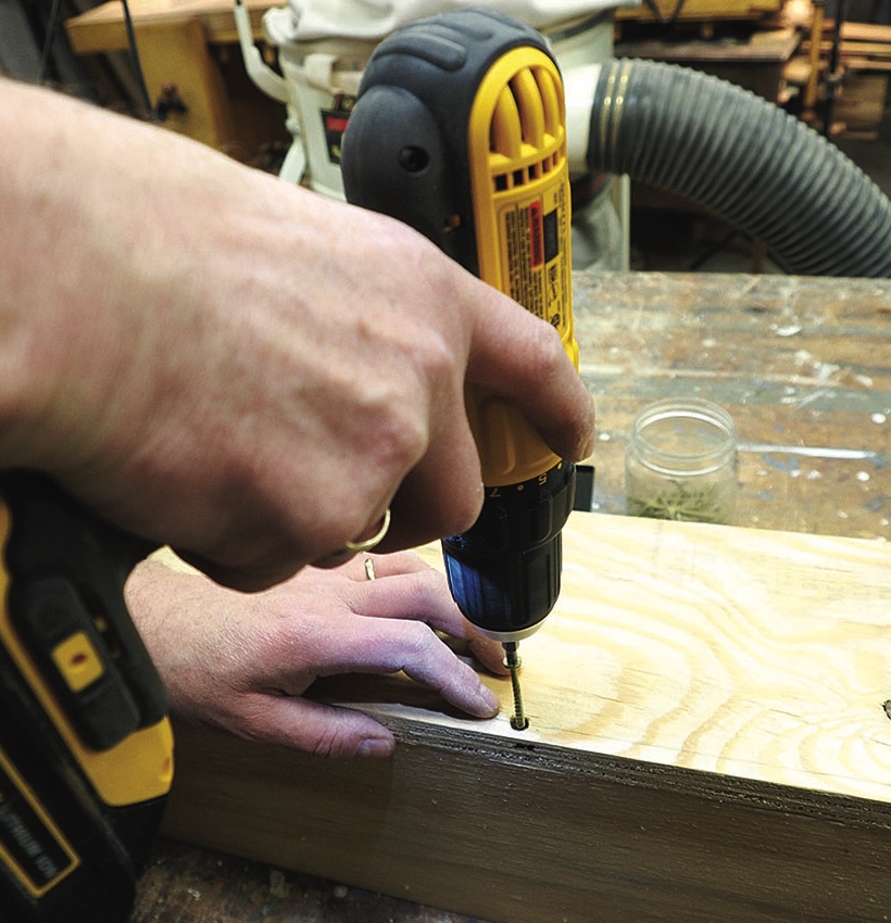 Person using electric screwdriver on wooden board.