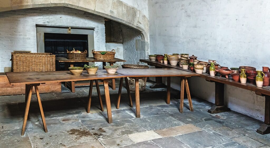 Medieval kitchen with pottery and baskets on tables.