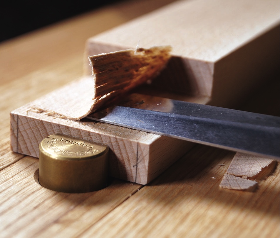 Wood chisel shaving hardwood edge on workbench.