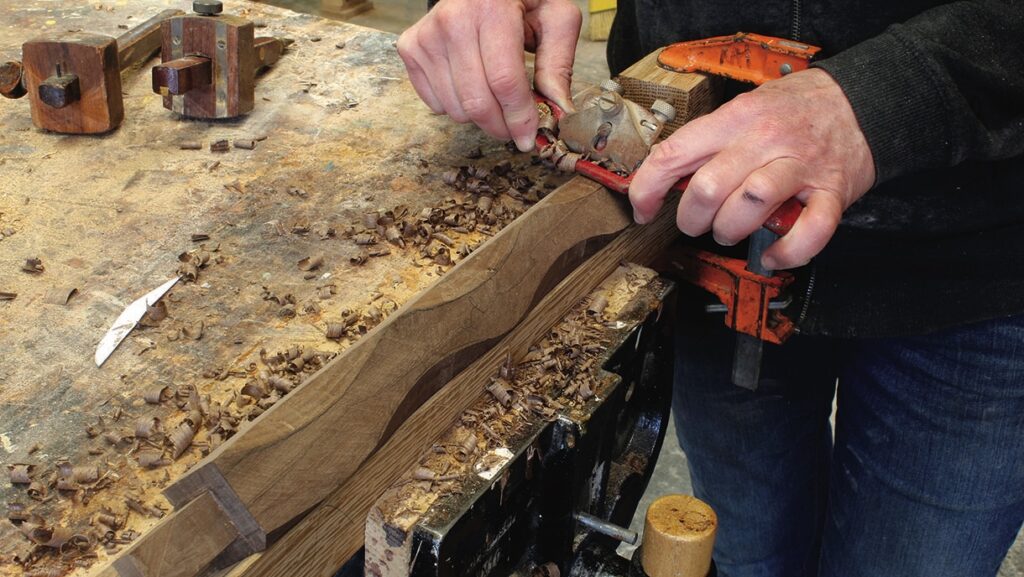 Craftsperson shaping wood with hand tool.