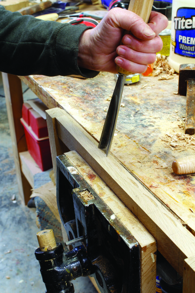 Person using chisel on wood in workshop.
