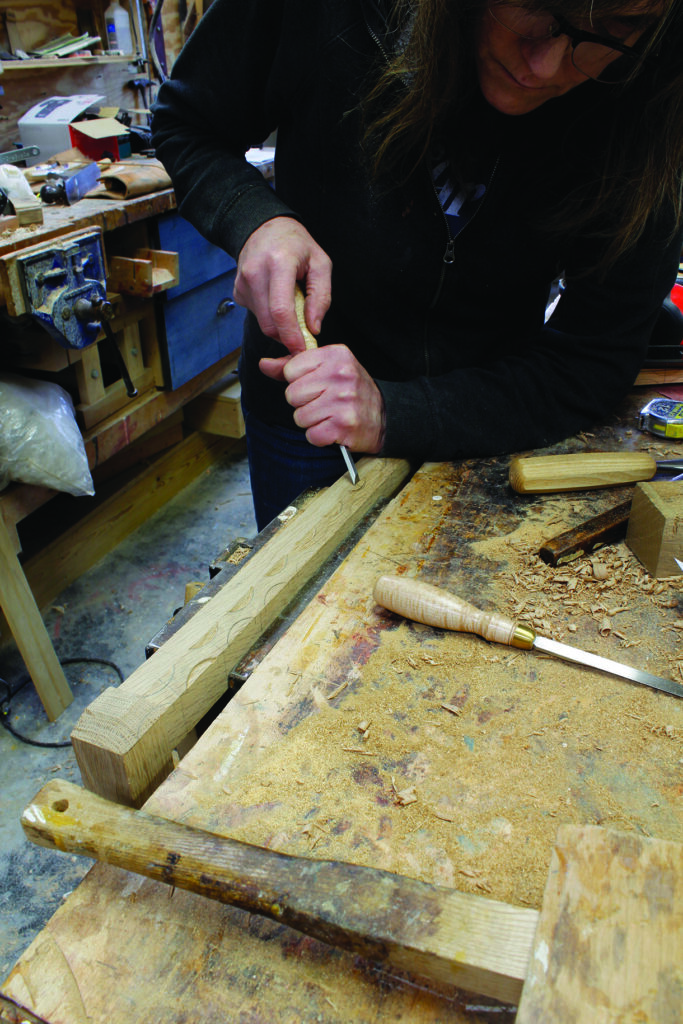 Person carving wood with chisel in workshop.