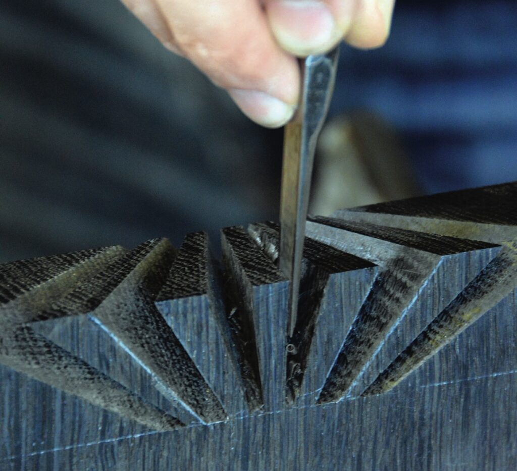 Craftsman carving intricate wood pattern with chisel.