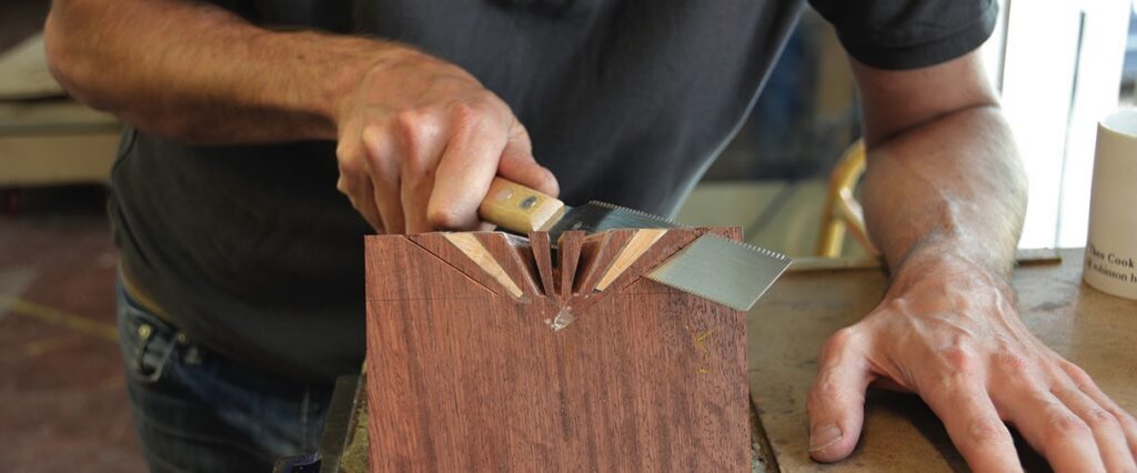 Person sawing wood for dovetail joint construction.