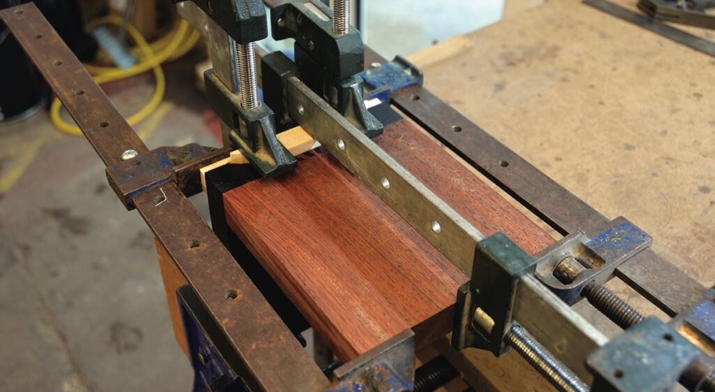 Woodworking clamps securing wooden piece on workbench.