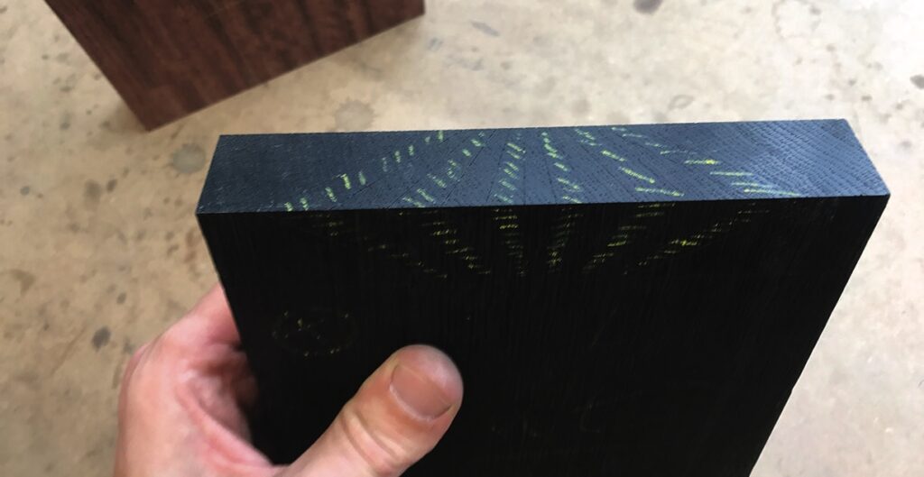 Hand holding dark wood block with green markings.