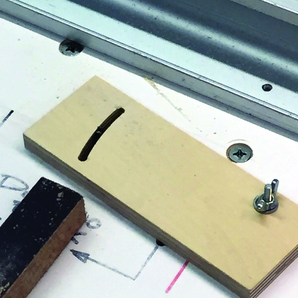 Wooden jig with slot and screw on surface.