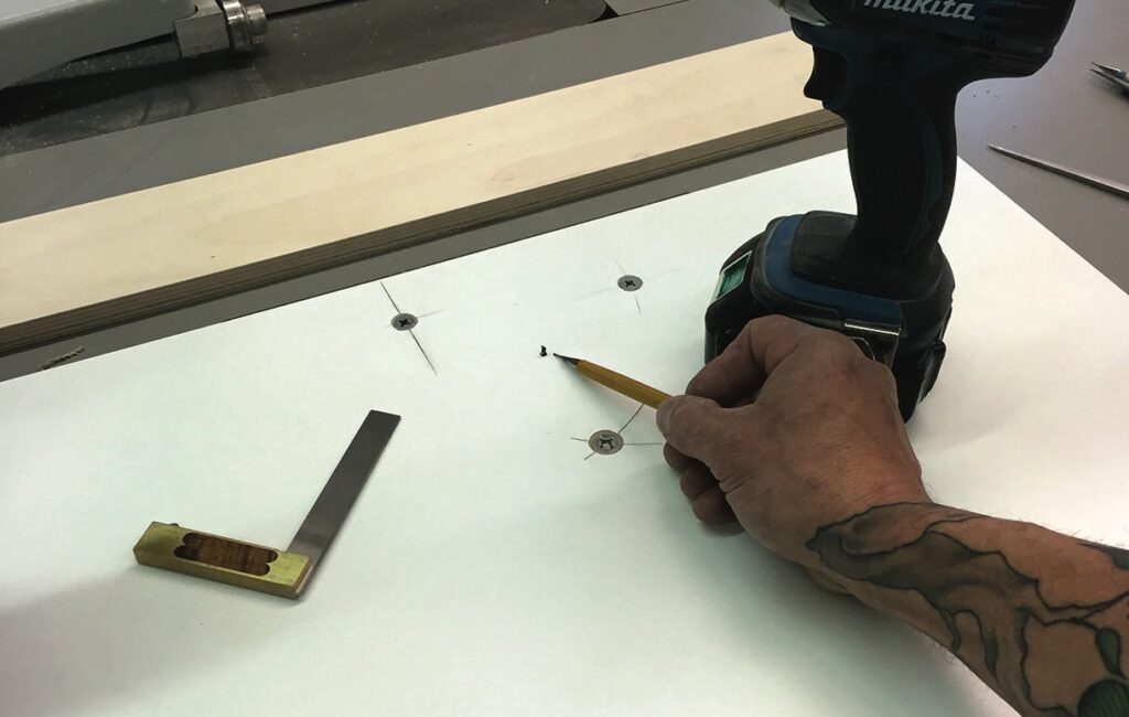 Person marking wooden board with drill and square.