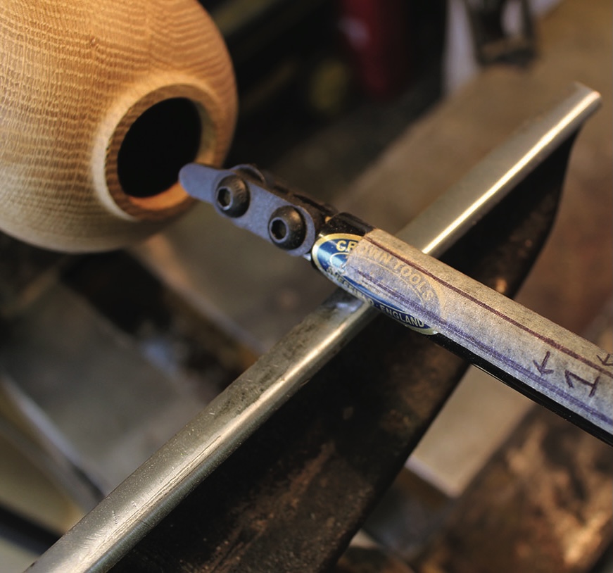 Woodturning tool shaping a wooden vase on lathe.