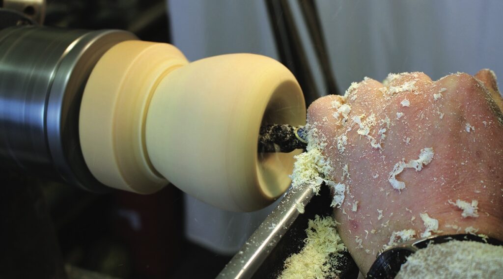 Person woodturning on lathe with wood shavings.