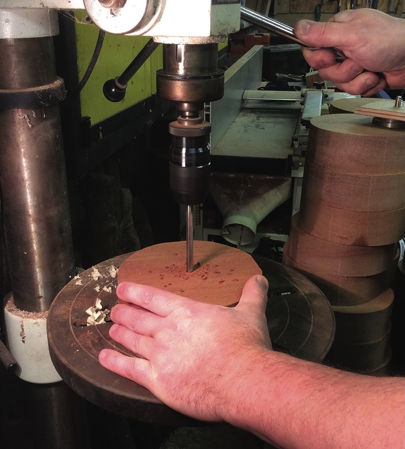 Person using a drill press on wooden disc.