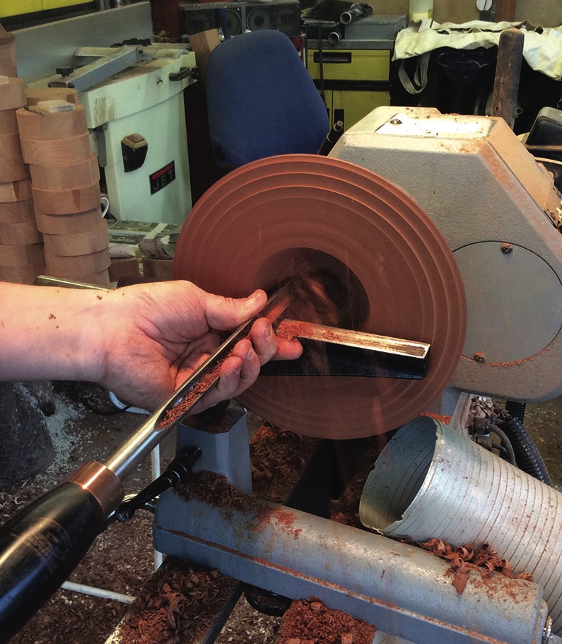 Person using lathe to shape wooden bowl.