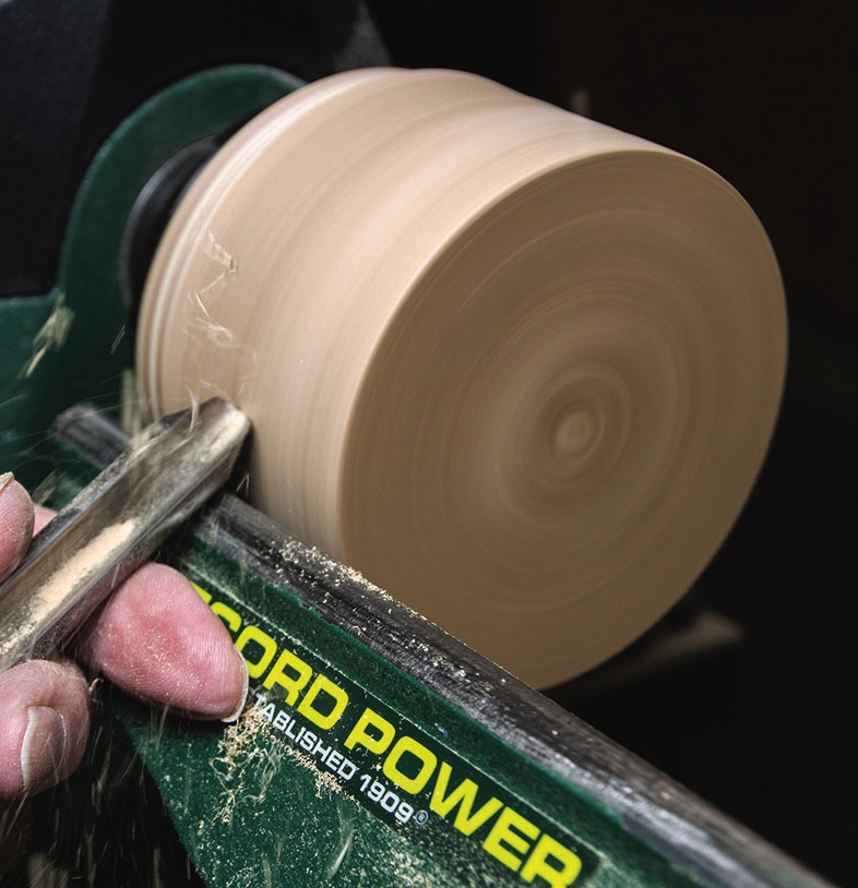 Person woodturning on lathe, creating wooden bowl.