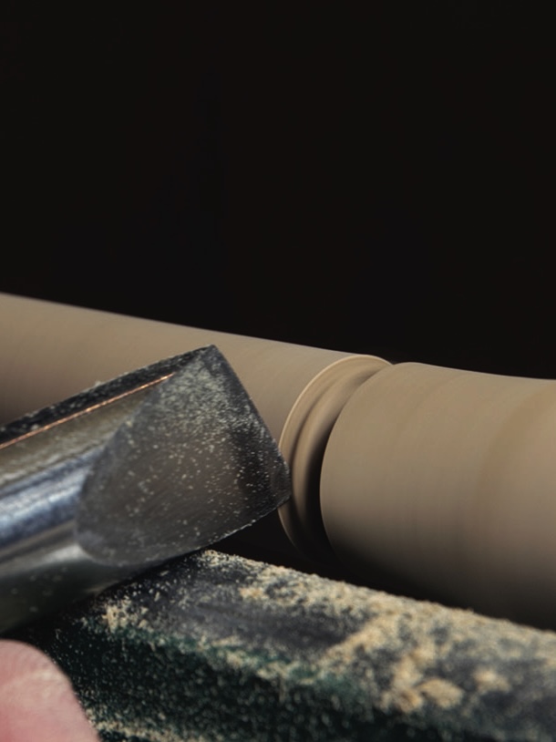 Woodturning tool shaping a wooden cylinder.