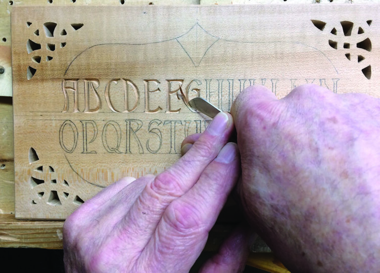 Hand carving alphabet on wood with gouge.