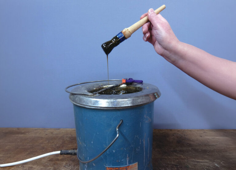 Person holding brush over blue metal bucket.