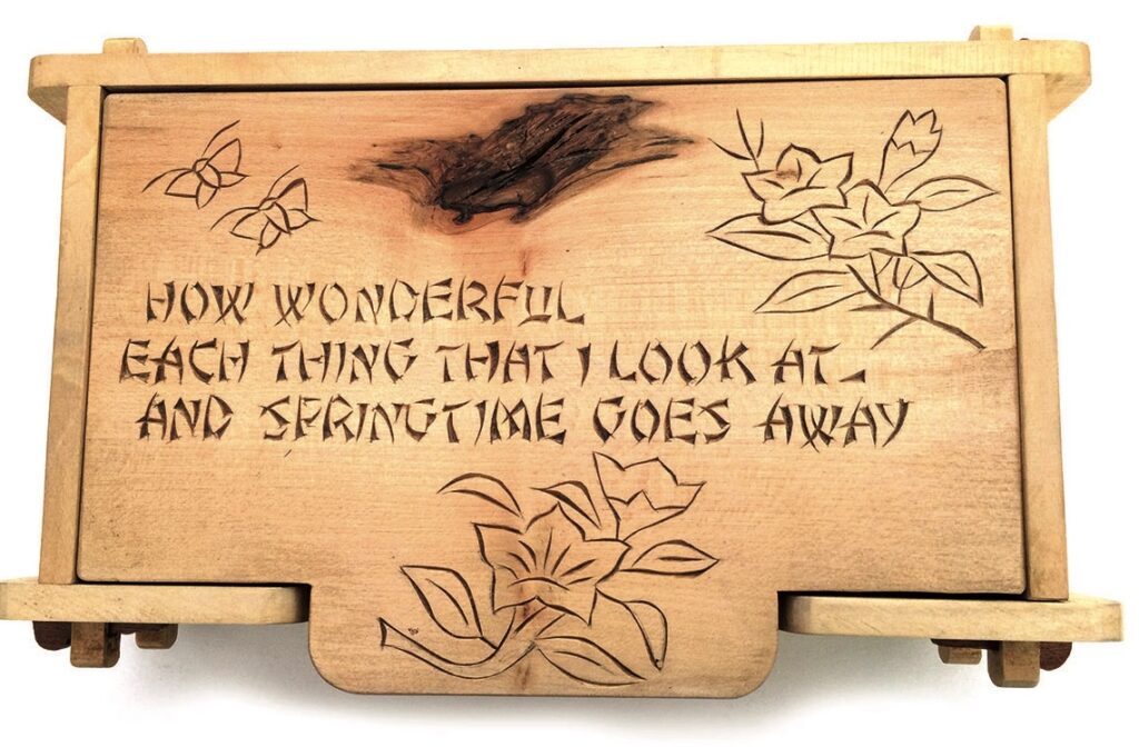 Wooden box with engraved poetry and flowers.