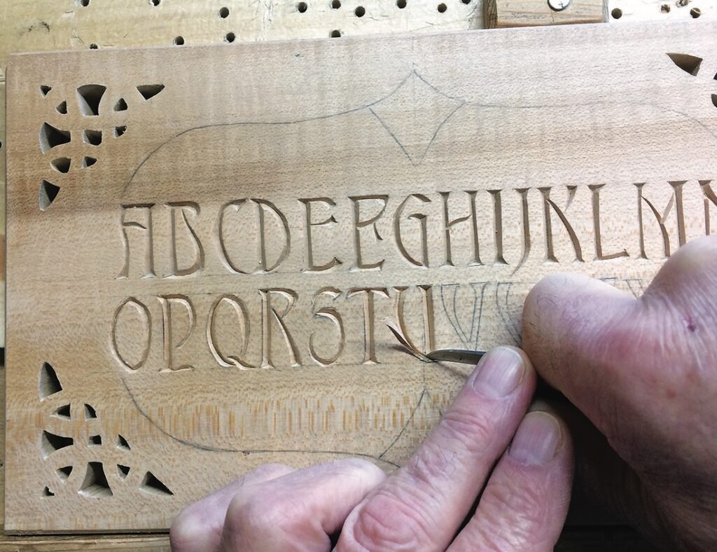 Hands carving letters into wooden block