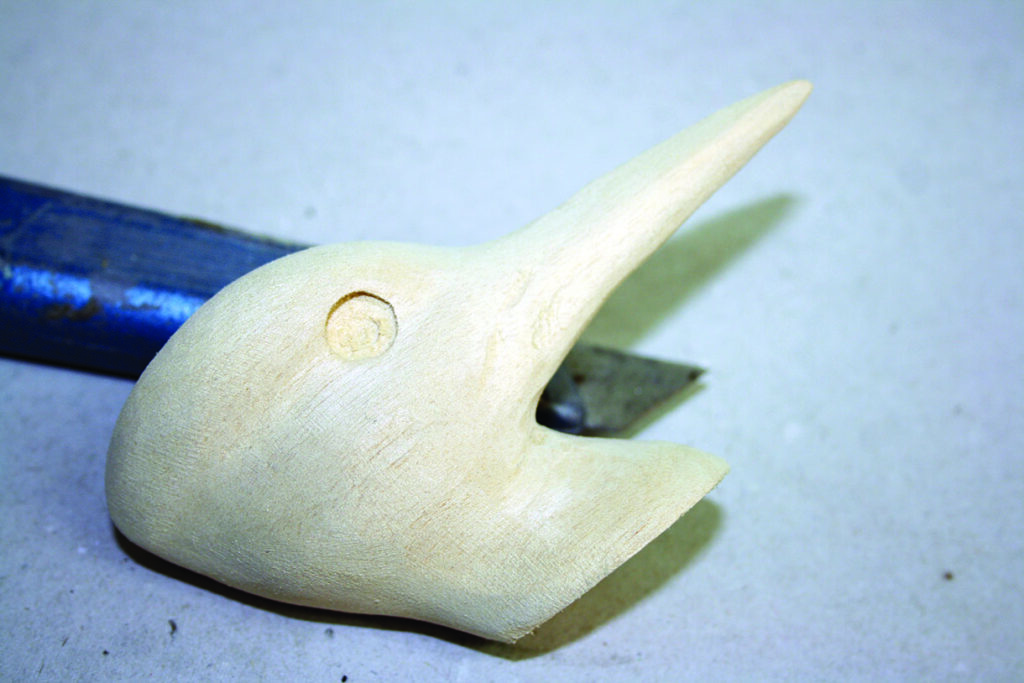Wooden bird head carving with a background tool.