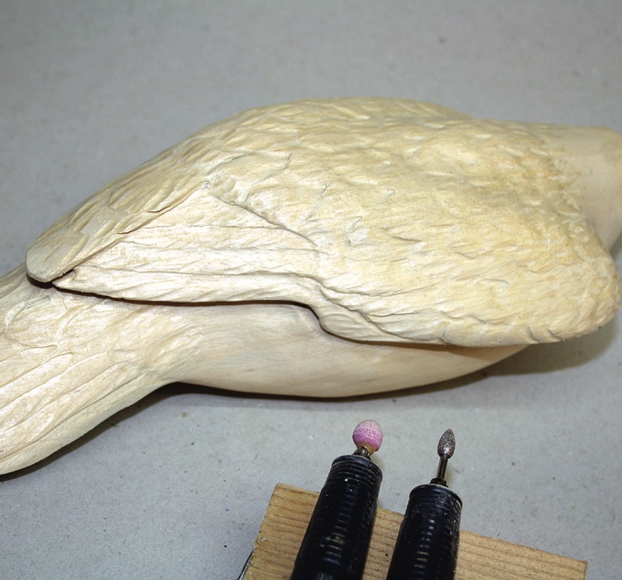 Wood carving of bird with engraving tools.