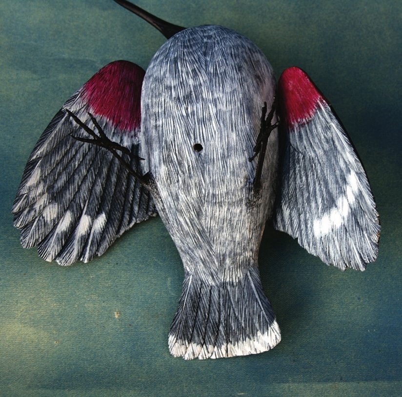 Handcrafted bird mask with grey and red feathers.