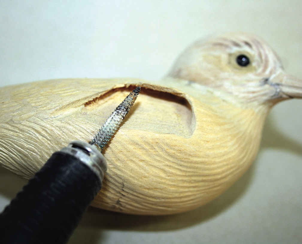 Carving tool creating wooden bird sculpture.