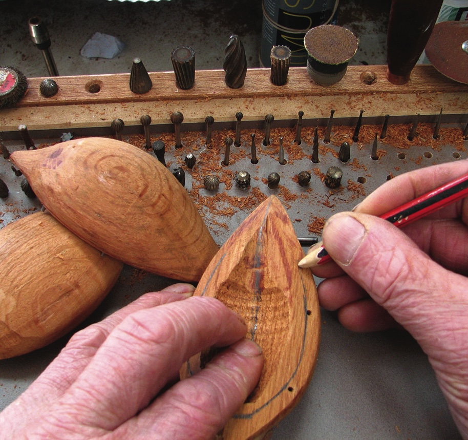 Craftsman marking wooden boat with pencil and drill bits.