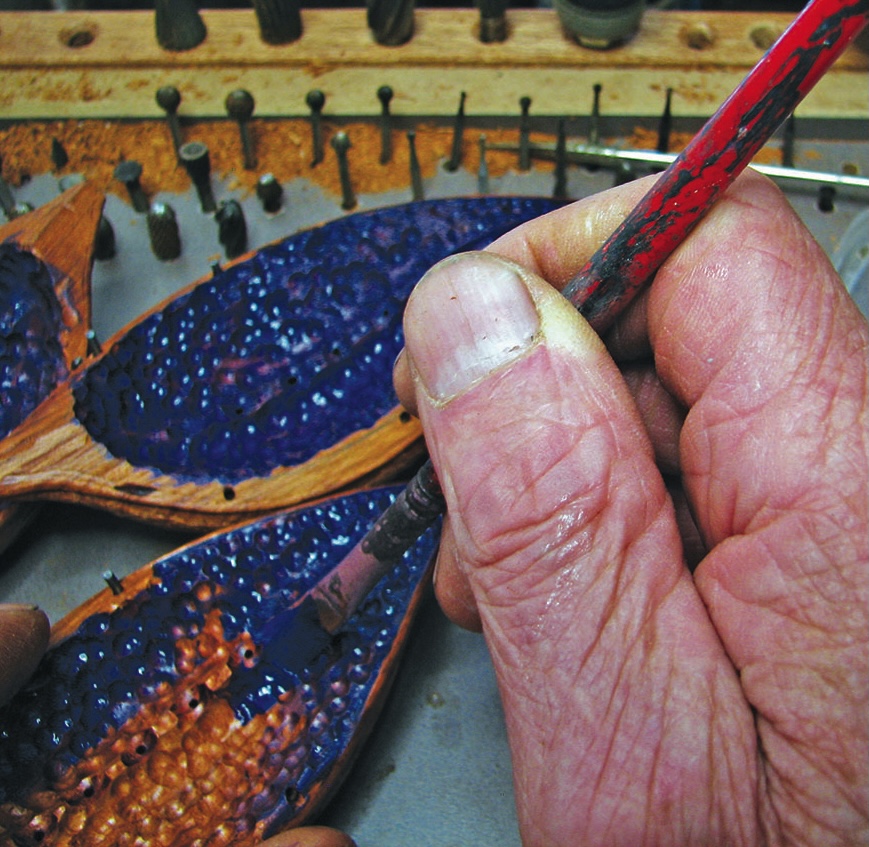 Person painting wooden sculpture with blue paint