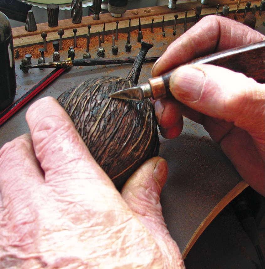 Hands carving intricate design on wooden object.