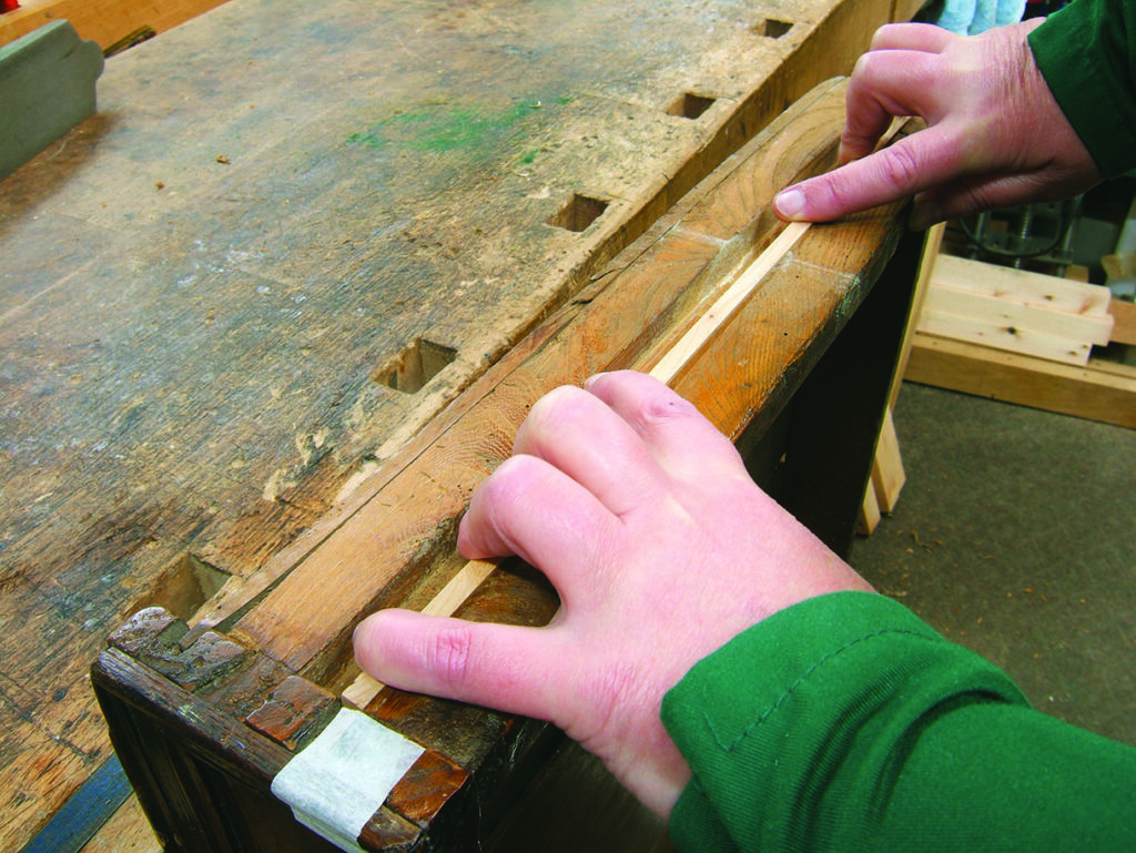 Hands using wooden plane on workbench.