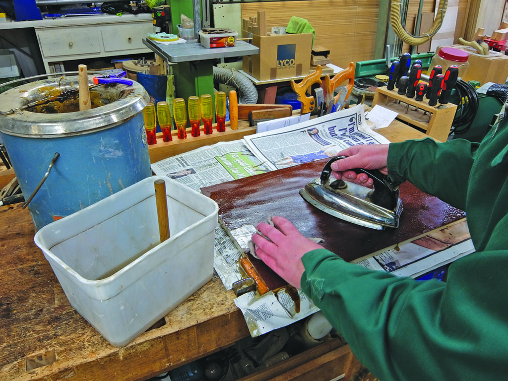 Person using iron on wood veneer in workshop.