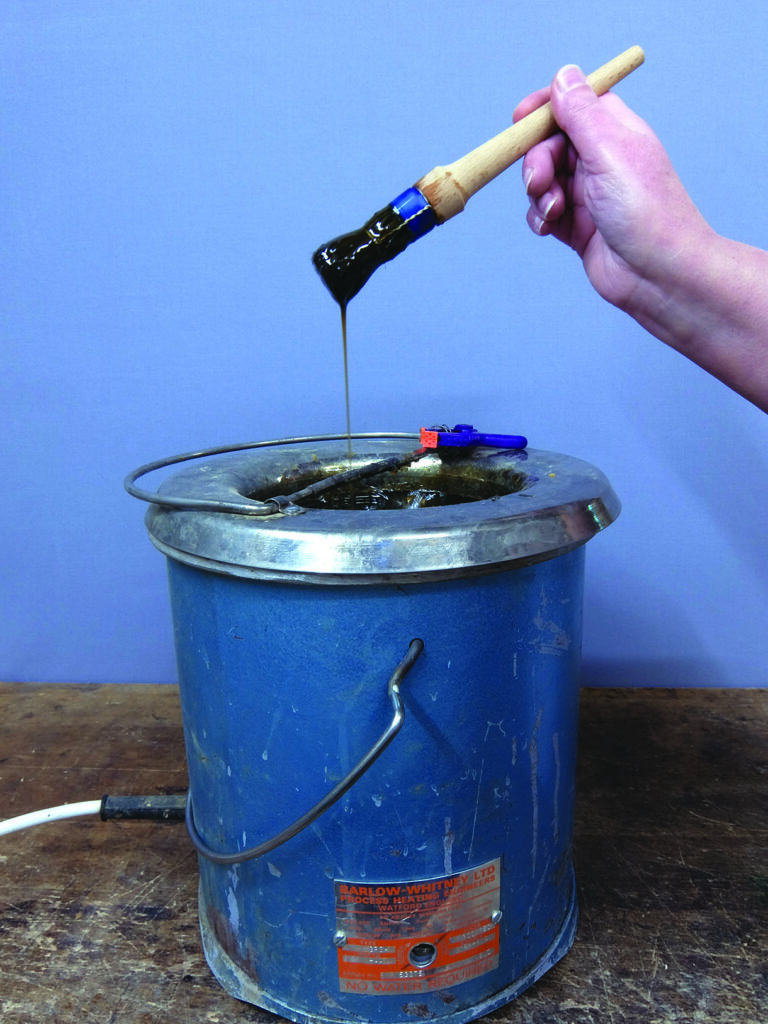 Hand dipping brush into hot glue pot.