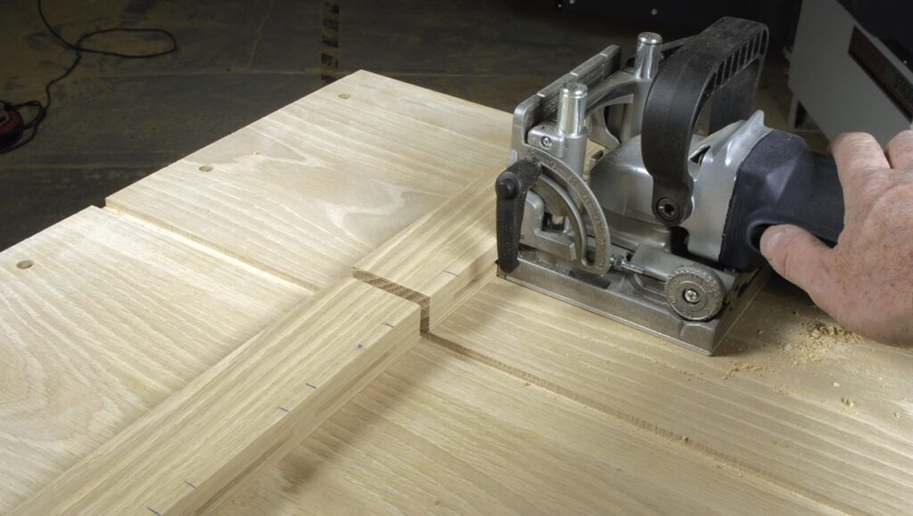 Carpenter using biscuit joiner on wooden board.