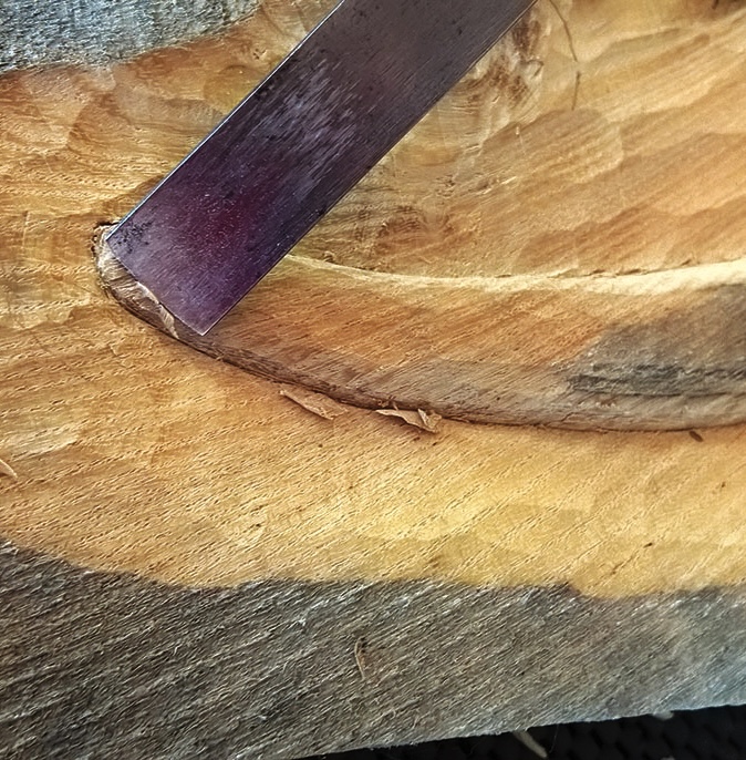 Chisel carving into wooden surface close-up.