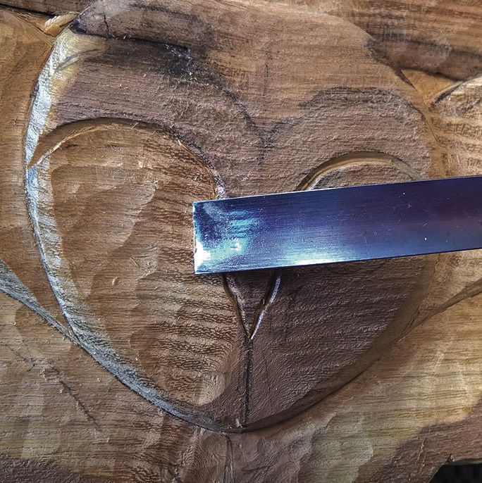 Carving owl face on wood with chisel tool.