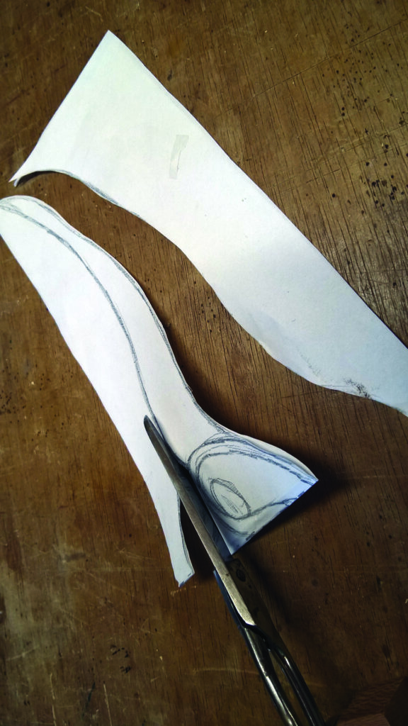 Scissors cutting paper with traced design on wood.
