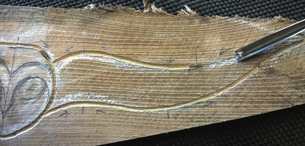 Wood carving with chisel on a wooden plank.