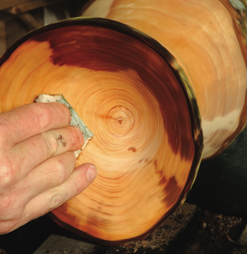 Hand sanding a wooden bowl on a lathe.