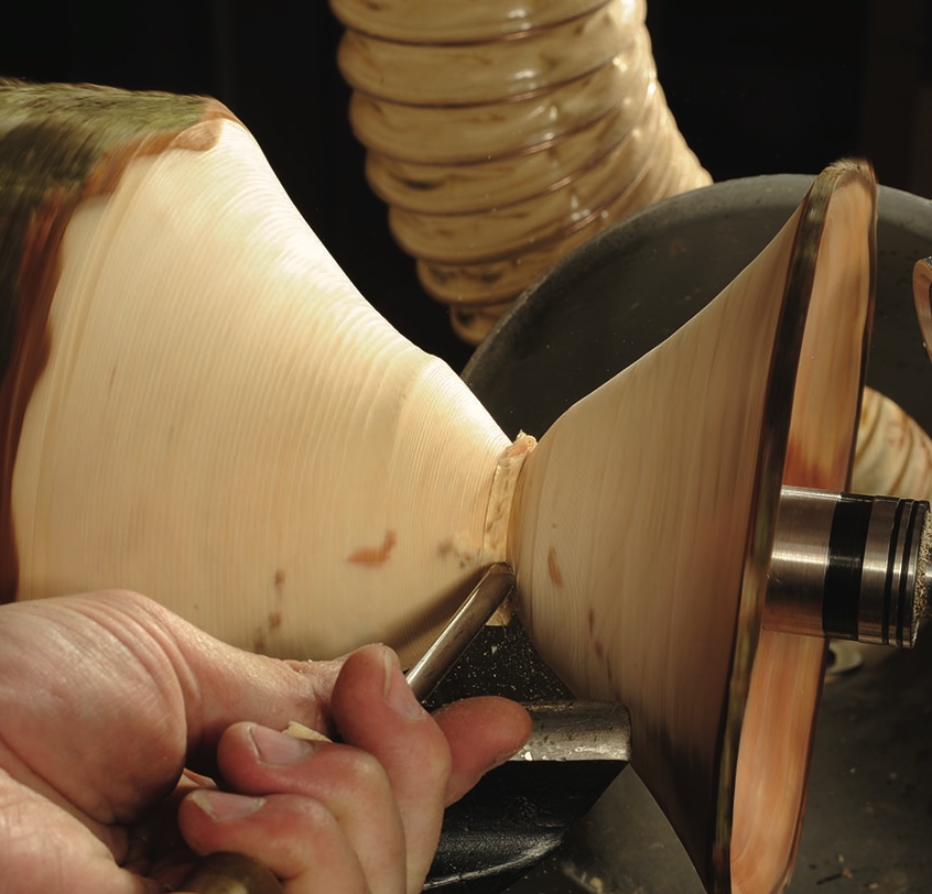 Woodturning process showing tool shaping wood piece.