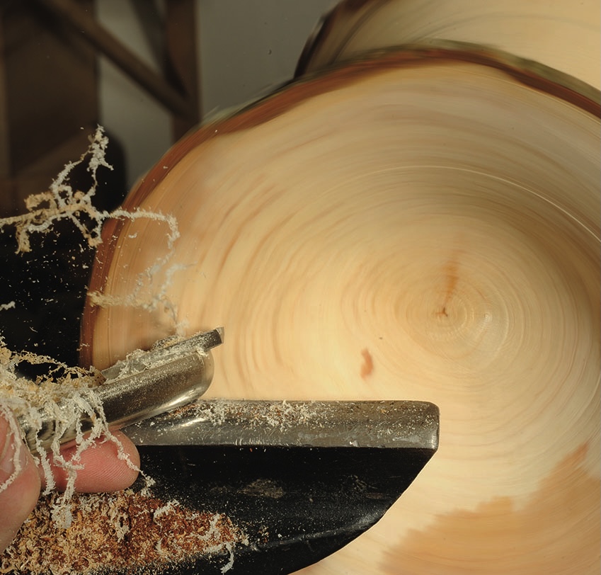 Woodturning with a lathe and tool shaving wood.