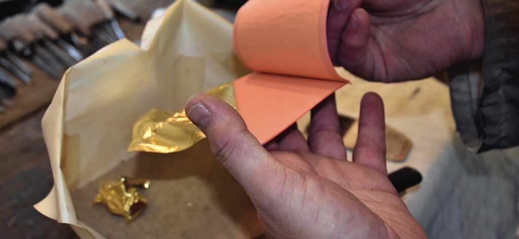Hands holding gold leaf sheets for crafting.