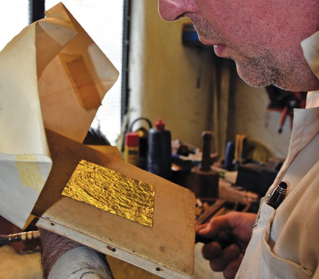 Man applying gold leaf in workshop.