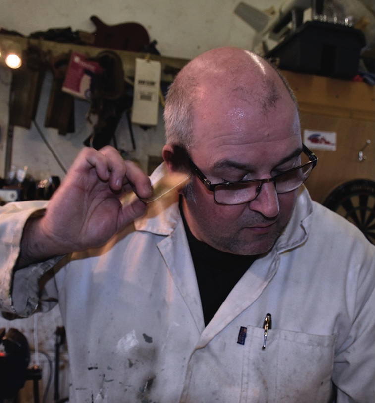 Man in workshop wearing white coat and glasses.
